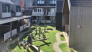 Ein Innenhof mit Spielplatz, ein Gebäude mit Balkon und eine Holzkonstruktion.