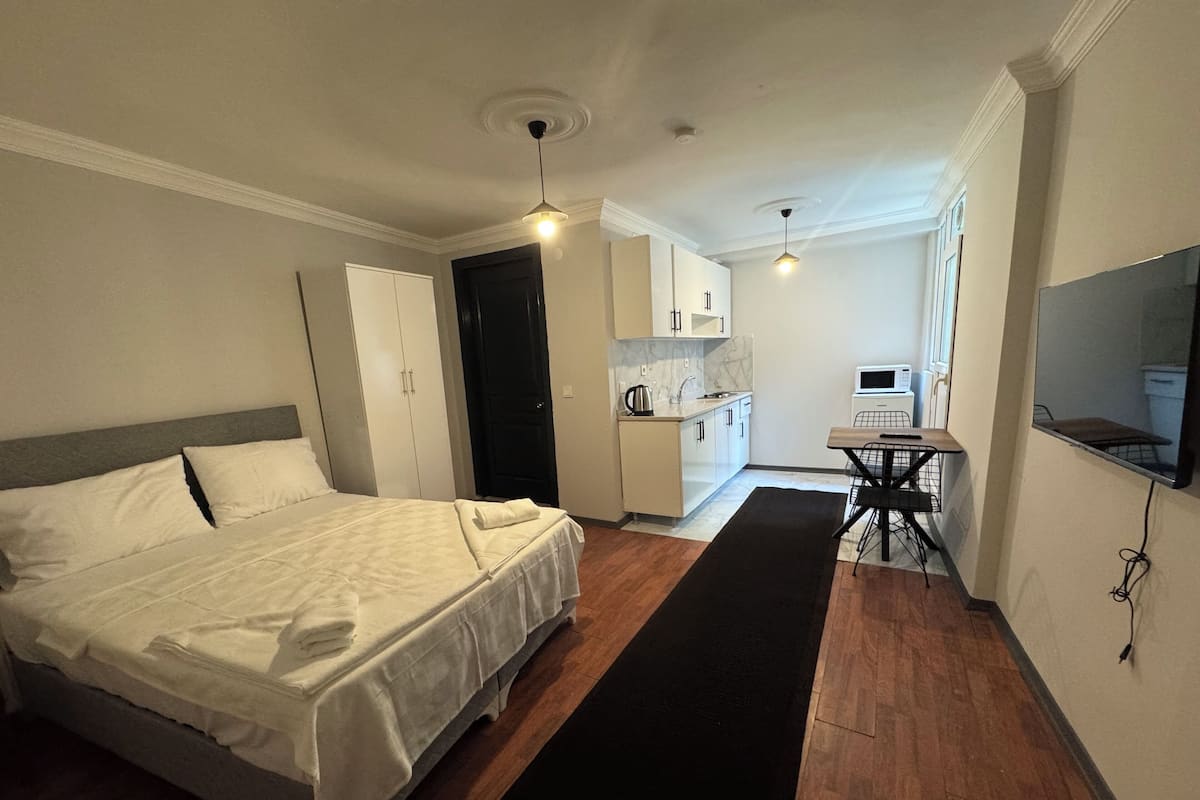 A hotel room with a bed, a desk, a kitchenette, and a TV.