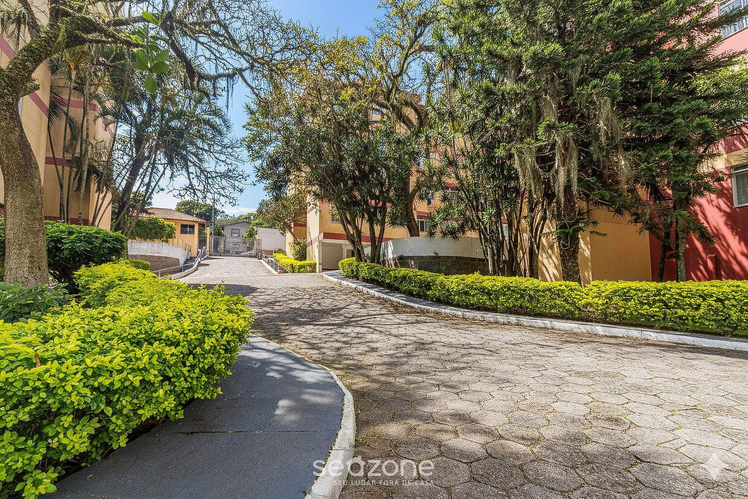A paved pathway flanked by neatly trimmed hedges and trees, leading towards a building with a red facade.