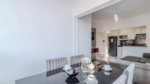 A modern dining area with a glass table, chairs, and a kitchen in the background. - Fully Furnished Apartments in Florianopolis - OPT (Florianópolis)