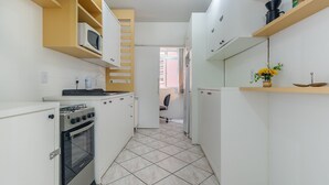 A compact kitchen with white cabinets, a microwave, a stove, and a refrigerator. - Fully Furnished Apartments in Florianopolis - OPT (Florianópolis)