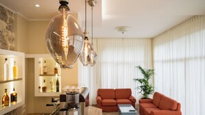 Una sala de estar moderna con un sofá rojo, una mesa de centro y una zona de cocina con una cafetera y estantes llenos de botellas.