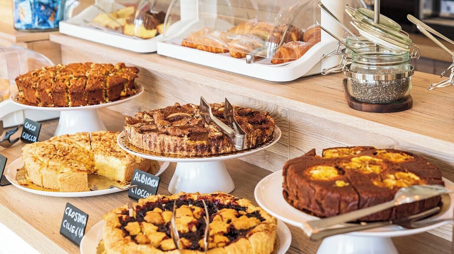 A variety of baked goods displayed on white stands with labels indicating different types of pastries.