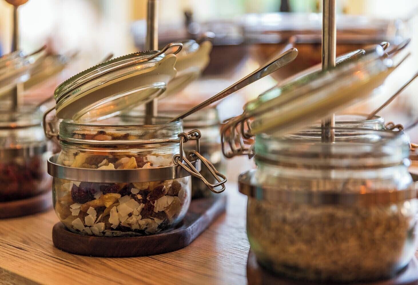 A row of glass jars with metal lids and handles, containing various food items, displayed on a wooden surface.