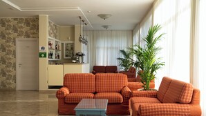 Una sala de estar con sofás naranja y blancos a cuadros, una mesita azul pequeña y una planta en maceta.