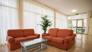 Un vestíbulo de hotel con dos sofás de cuadros naranja, una mesa de centro de vidrio y una planta grande en maceta.