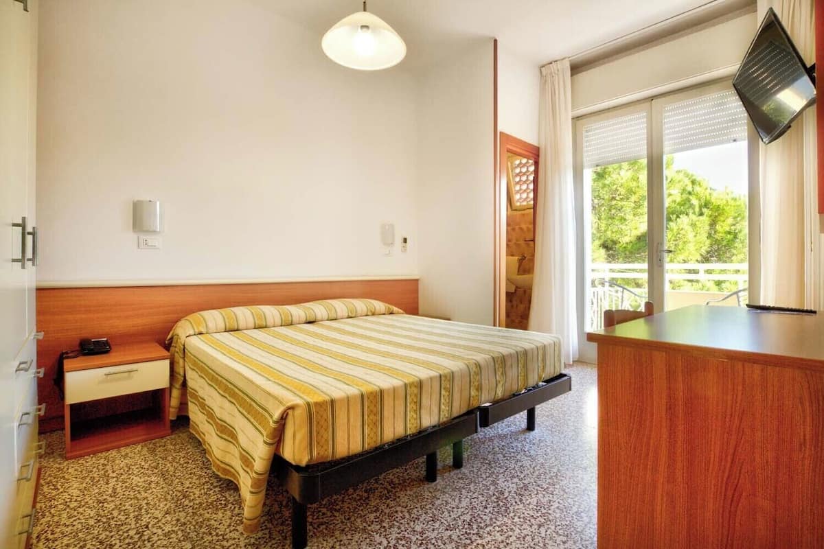 A hotel room with a bed, bedside table, and a desk with a chair.