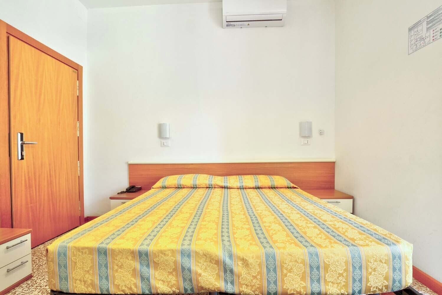 Habitación de hotel con cama, armario de madera, mesitas de noche y aire acondicionado.