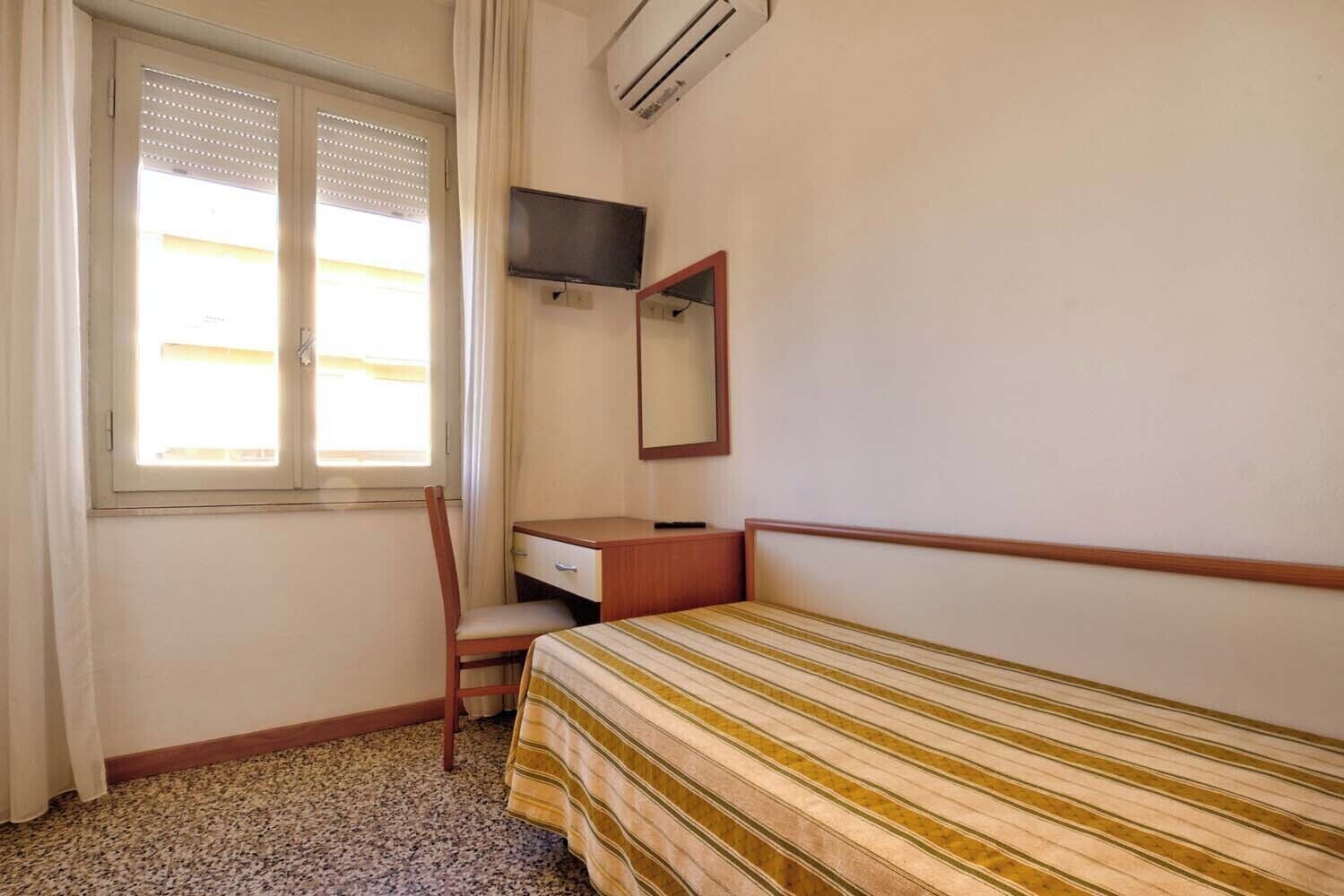Een kleine, eenvoudige kamer met een bed, een bureau, een stoel en een televisie.