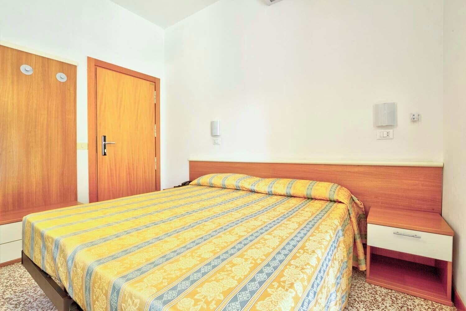 A hotel room with a bed, a wooden wardrobe, and a nightstand.