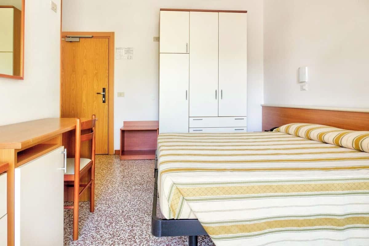 A bedroom with a bed, a wooden desk, and a wardrobe.
