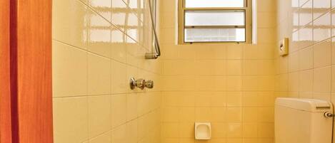 Un baño pequeño con baldosas amarillas, ducha, inodoro y ventana.