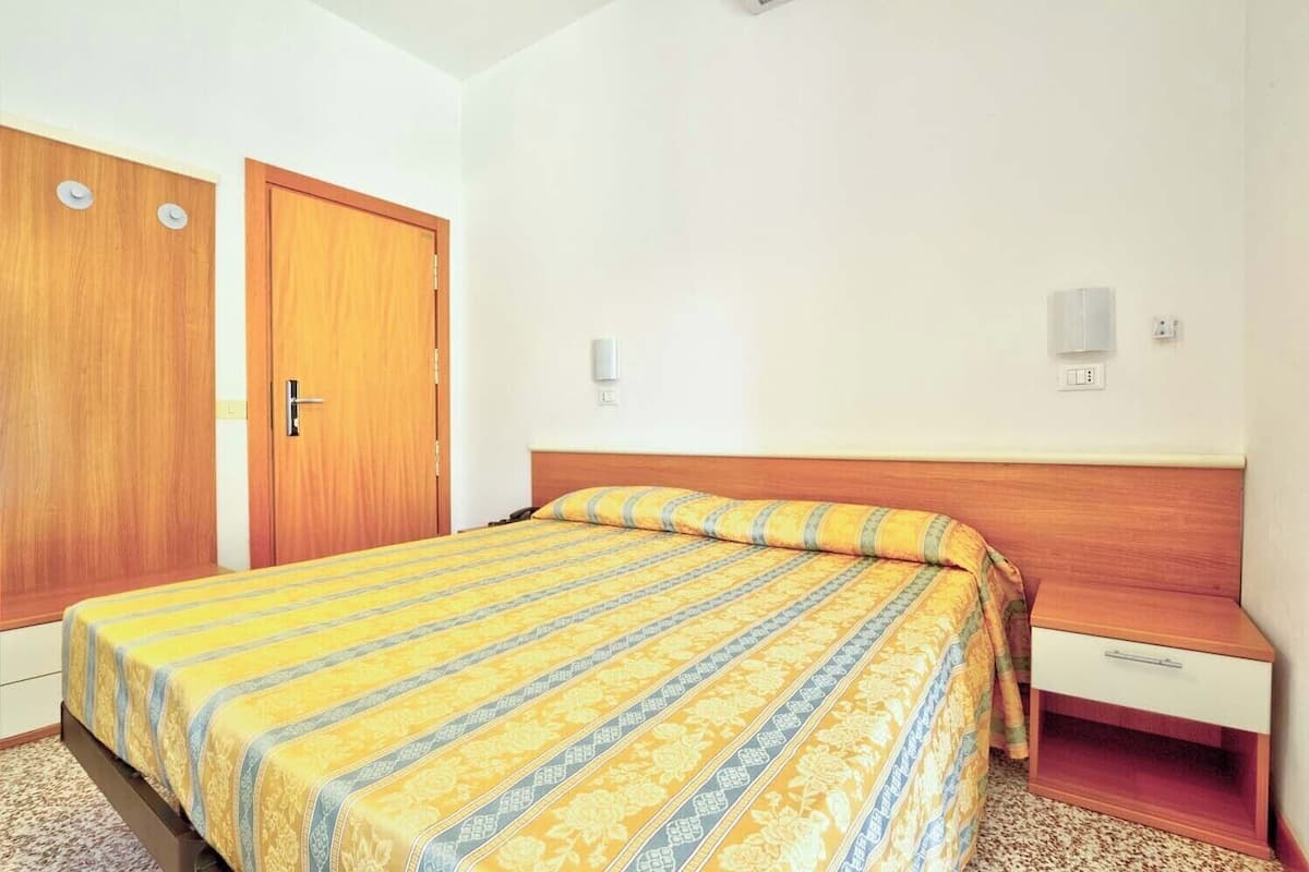 A hotel room with a bed, a wooden wardrobe, and a small bedside table.