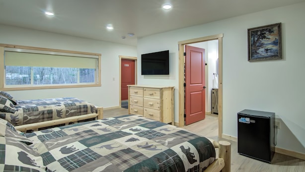 A bedroom with two beds, a dresser, a TV, and a refrigerator.
