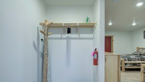 A bedroom with a wooden bed, a small wooden desk, and a wall-mounted shelf with a fire extinguisher.