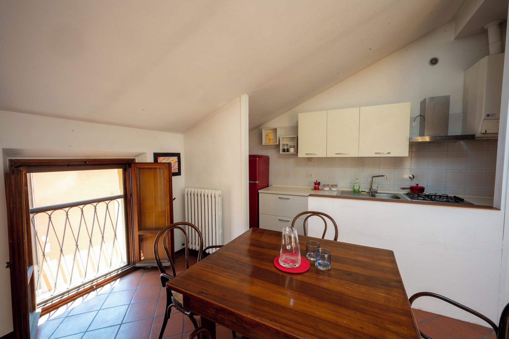 A compact kitchen with white cabinets, a red refrigerator, and a tiled backsplash.