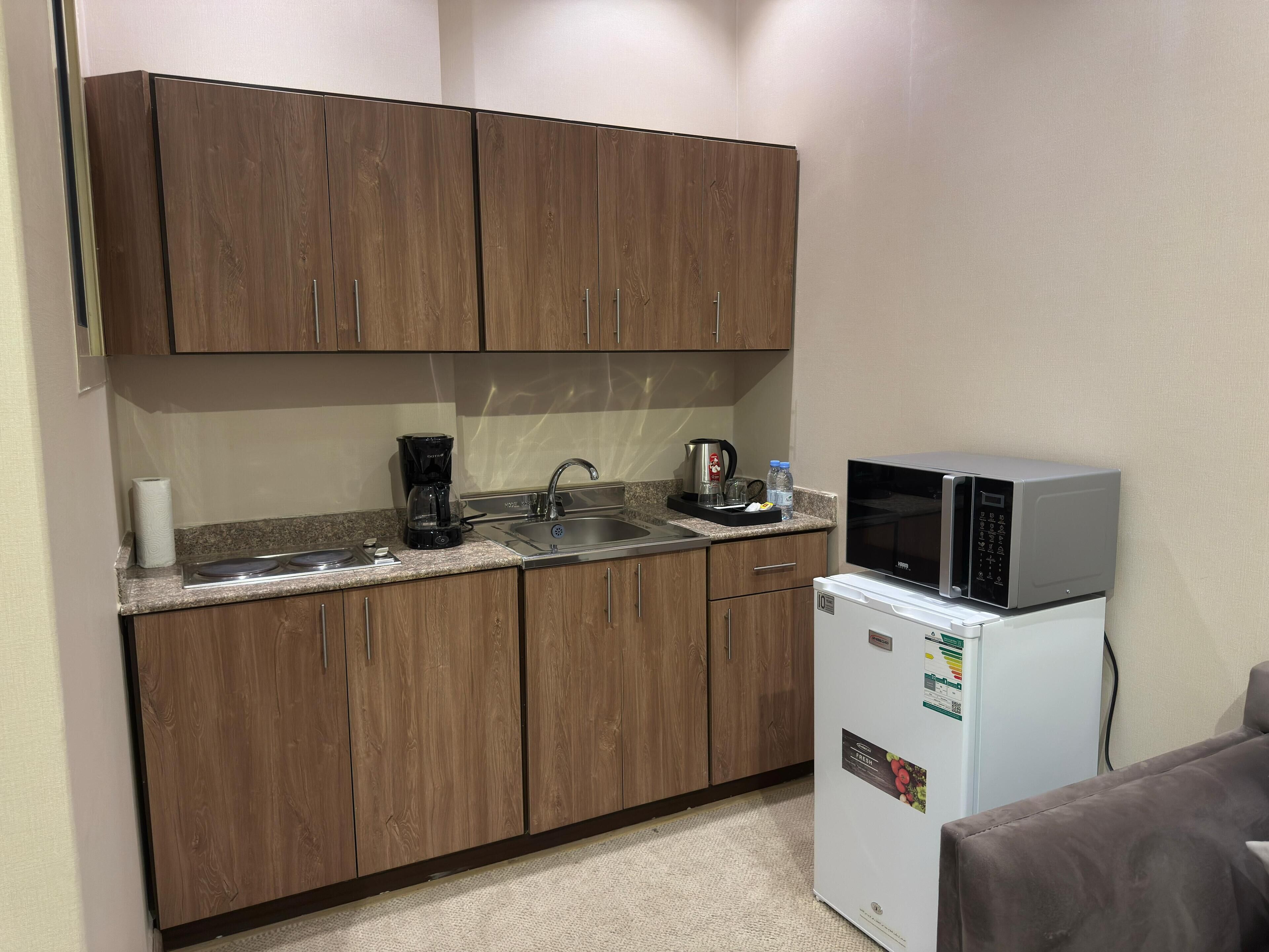Una cocina compacta con armarios de madera, un lavamanos, una cafetera, un microondas y un refrigerador.