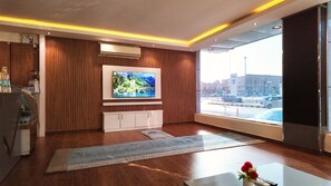 Un soggiorno moderno con televisione a schermo piatto, pareti rivestite in legno, un'ampia finestra vista città e una macchina per il caffè.