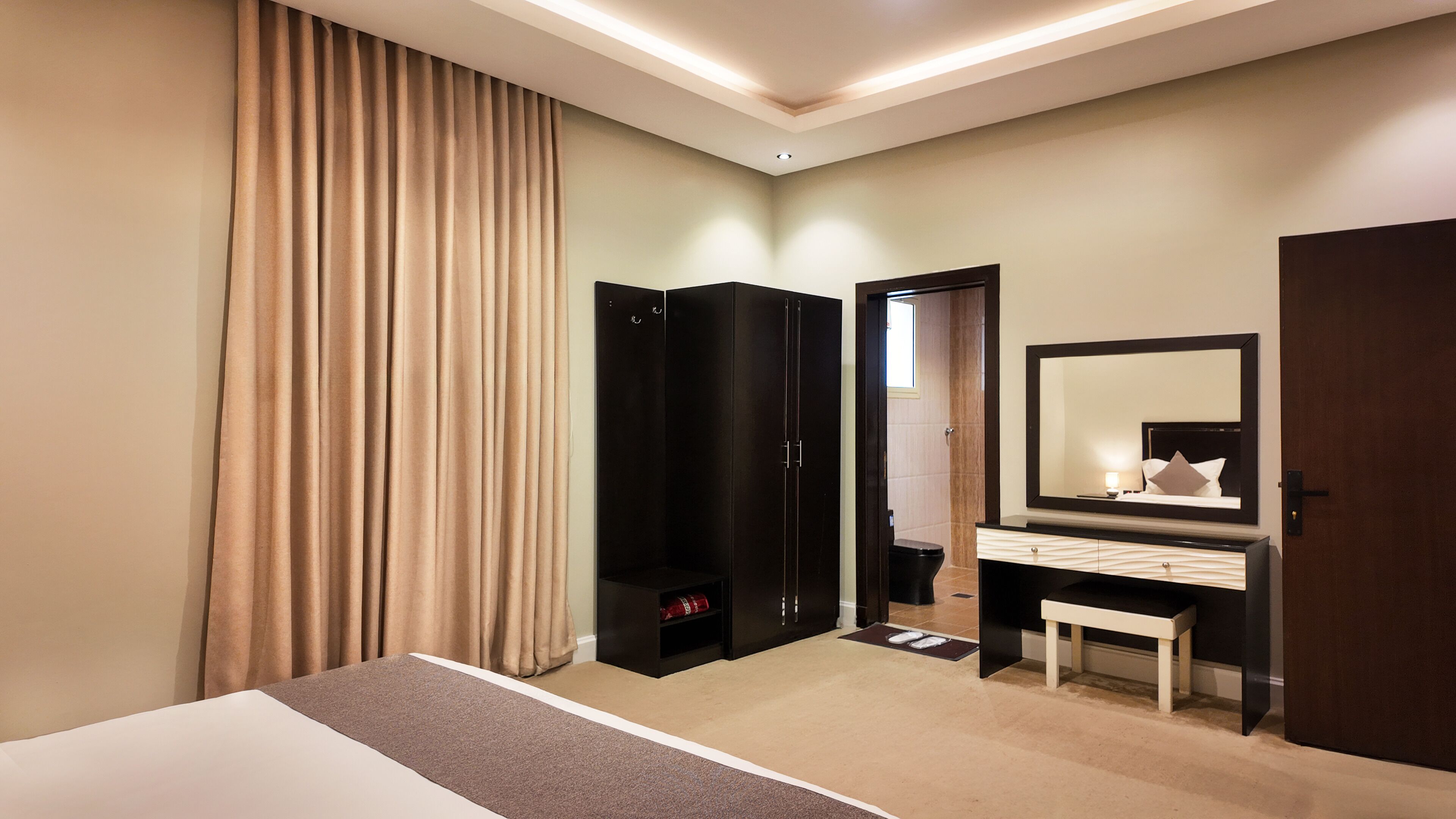 A hotel room with a bed, a vanity with a mirror, a wardrobe, and a bathroom door.