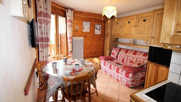 Una habitación acogedora tipo cabaña, con una mesa de comedor, sillas, un sofá, armarios de madera y una televisión.