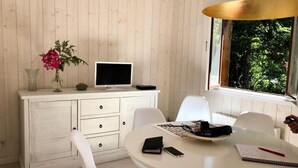 A room with a white wooden cabinet, a round table, and a window with a view of greenery. - Chalet With Garden Near French Coast (Hourtin)