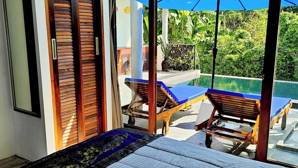 Ein Schlafzimmer mit einem großen Bett, Blick auf einen Pool und einer Schiebetür.
