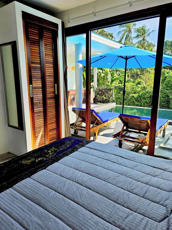 Ein Schlafzimmer mit einem großen Bett, Blick auf einen Pool und einer Schiebetür.