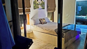 Ein Schlafzimmer mit einem Bett, einem Nachttisch, einem Fenster und Blick ins Freie.
