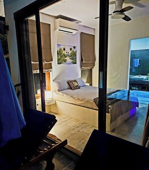 Ein Schlafzimmer mit einem Bett, einem Nachttisch, einem Fenster und Blick ins Freie.