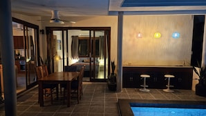 Ein moderner Poolbereich im Innenbereich mit Esstisch und Stühlen, einer Bar mit Hockern und einem Deckenventilator.