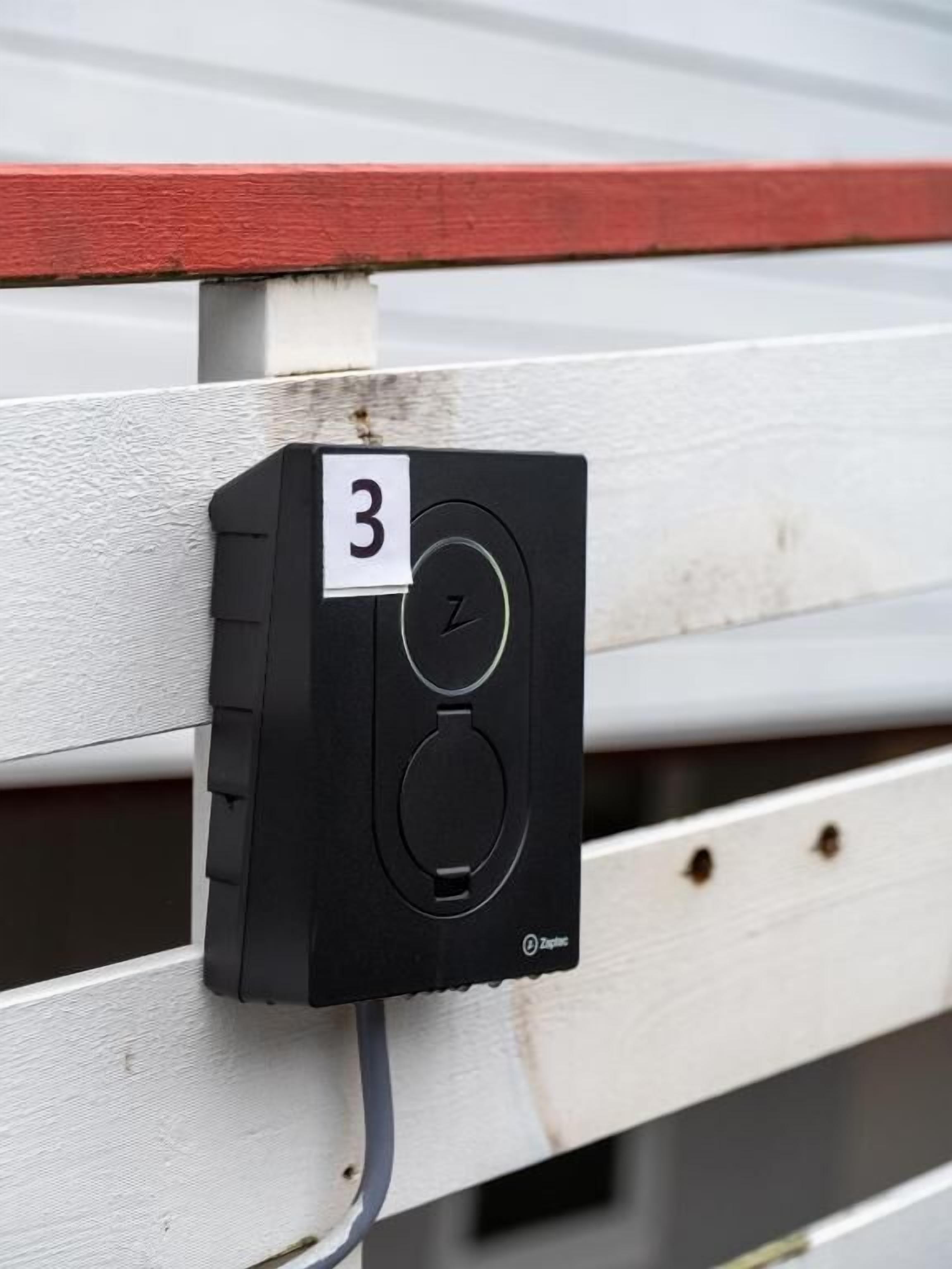 Un dispositivo de seguridad negro con el número 3, adherido a una valla de madera blanca.