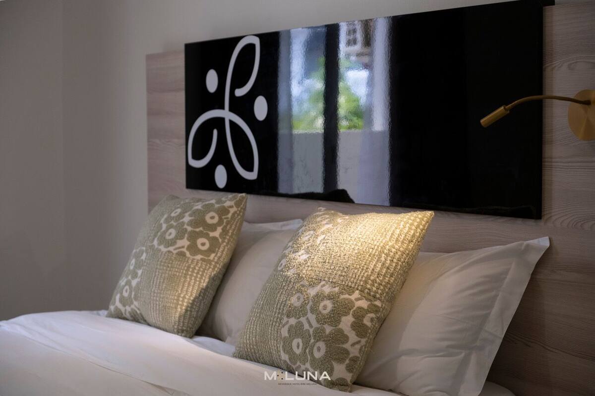 Ein Schlafzimmer mit einem Bett, zwei Zierkissen, einem Wandbild und einer Nachttischlampe.