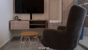 Ein modernes Zimmer mit einem an der Wand montierten Flachbildfernseher, einem Holznachttisch, einem grauen Sessel und einer Glastrennwand.
