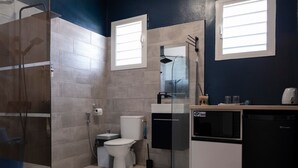 Ein modernes Badezimmer mit Duschkabine aus Glas, Toilette, Waschbecken und einem kompakten Geschirrspüler.