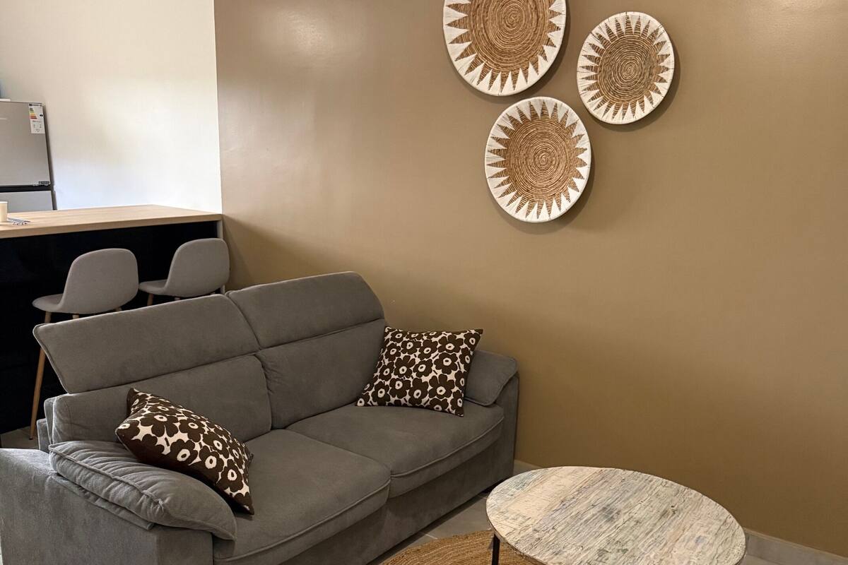 Ein modernes Wohnzimmer mit einem grauen Sofa, gemusterten Kissen, einem runden Couchtisch und drei dekorativen Wandtellern.