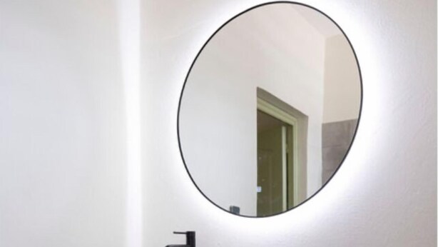 A modern bathroom with a white vessel sink, black countertop, wooden cabinet, and a round mirror with a black frame. - Meluna (Mamoudzou)