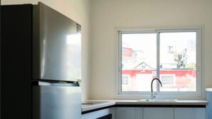 Eine moderne Küche mit einem Edelstahl-Kühlschrank, einem Geschirrspüler und einem Fenster mit Blick auf umliegende Gebäude.