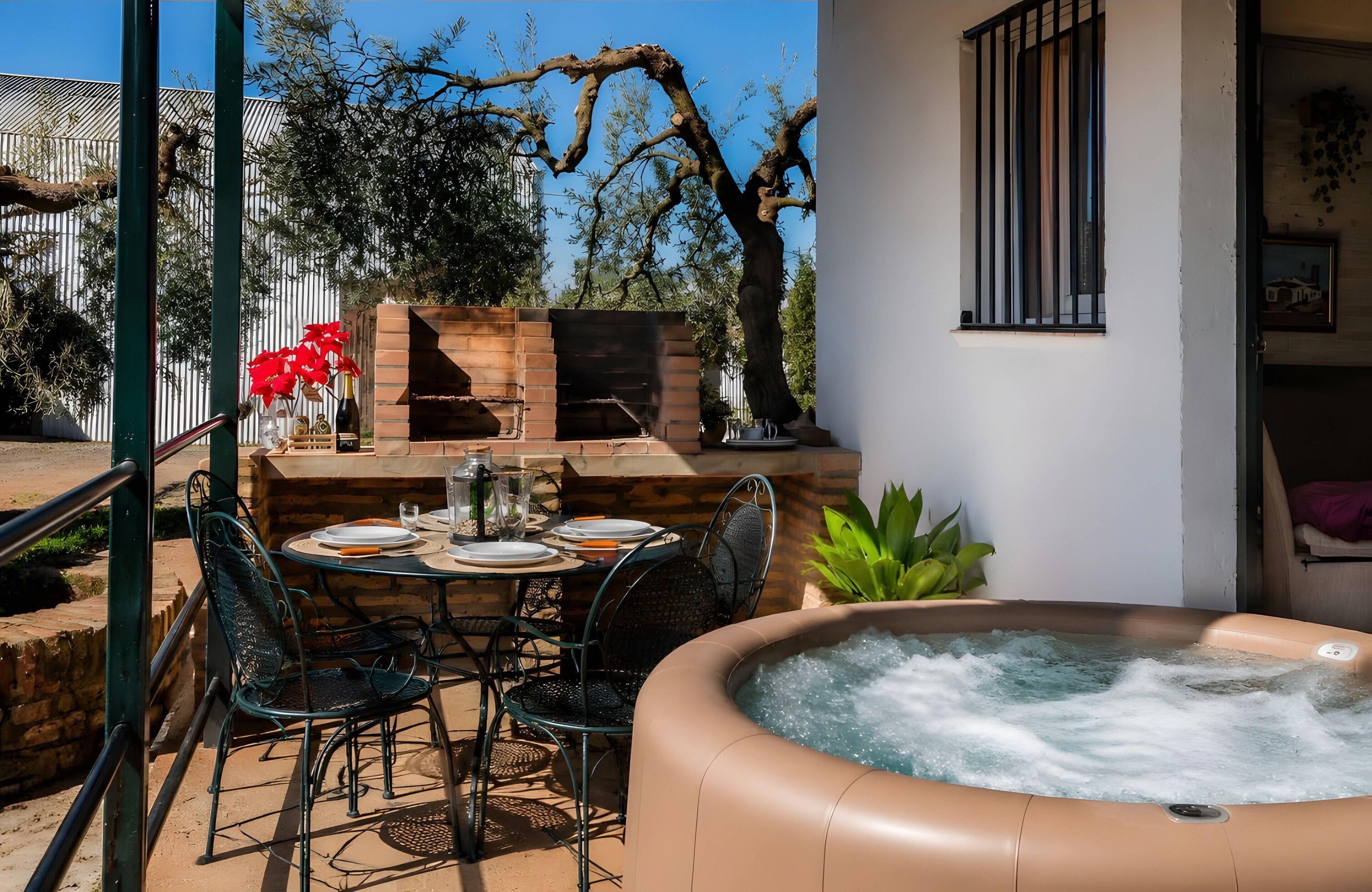 Une terrasse extérieure avec un jacuzzi, un barbecue en briques et une table à manger pour deux personnes.