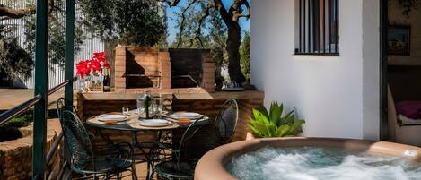 Une terrasse extérieure avec un jacuzzi, un barbecue en briques et une table à manger pour deux personnes.