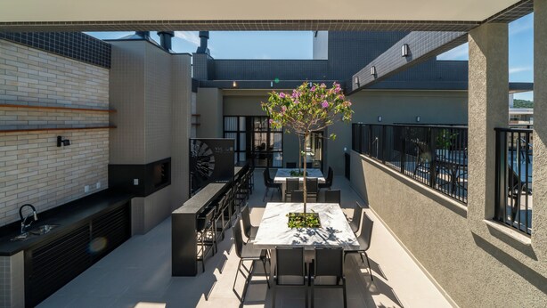 An outdoor patio with a dining table, chairs, and a flower arrangement. There is a grill and a seating area with a view of the sky. - APTO flat em condomínio com piscina B (Bombinhas)