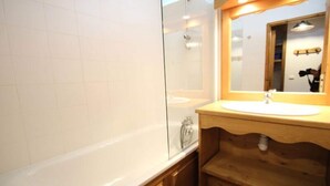 Un baño con una bañera blanca, un tocador de madera con un lavabo y un espejo sobre el lavabo.