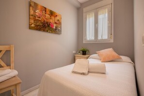A bedroom with a bed, a nightstand with a plant, a window with curtains, and a painting on the wall. - Apartment 'Lovely in Triana' with Wi-Fi and Air Conditioning (Sevilla)