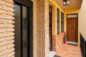 Un edificio con fachada de ladrillo, una puerta negra, una puerta de madera y un área de entrada con azulejos.