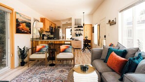 Ein modernes Wohnzimmer mit einer Couch, Sesseln, einem Couchtisch und einer Küche im Hintergrund.