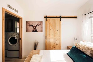 Ein Schlafzimmer mit einem Bett, einer Holztür, die sich schieben lässt, einer Waschmaschine und einem gerahmten Bild eines Elches.