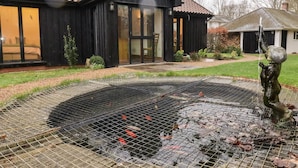 Ein Haus mit schwarzem Anstrich, einem Ziegeldach und einem Koiteich im Vorgarten.
