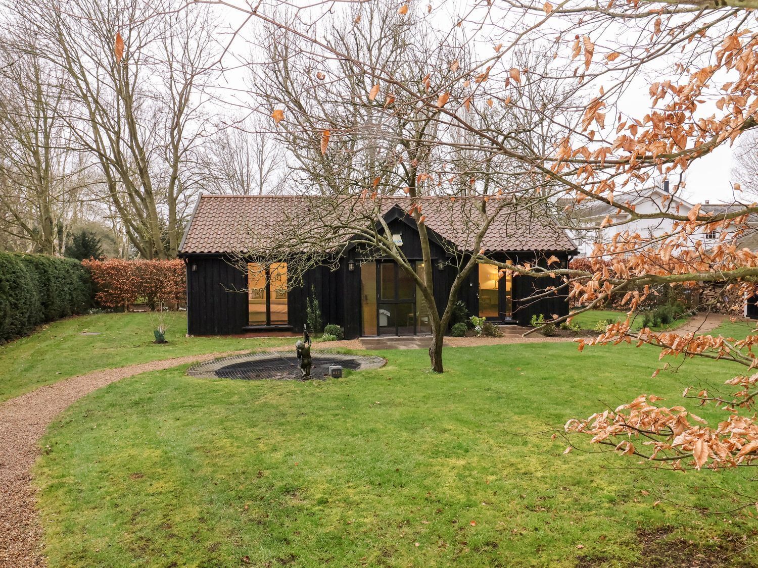 Une maison rustique en bois, avec un toit en tuiles, une allée circulaire et un petit jardin agrémenté d’une fontaine.