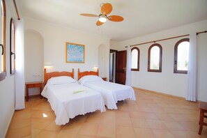 Camera d'albergo con due letti singoli, una ventola a soffitto, un quadro appeso e vista attraverso finestre ad arco.