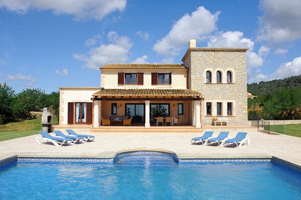 Una casa su due piani con piscina, un patio con poltrone relax e una torre in pietra.