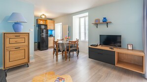 A modern living room with a dining area, a kitchen in the background, and a TV on a wooden stand. - Furnished Apartment in Townhouse, City Center Location (Jonzac)
